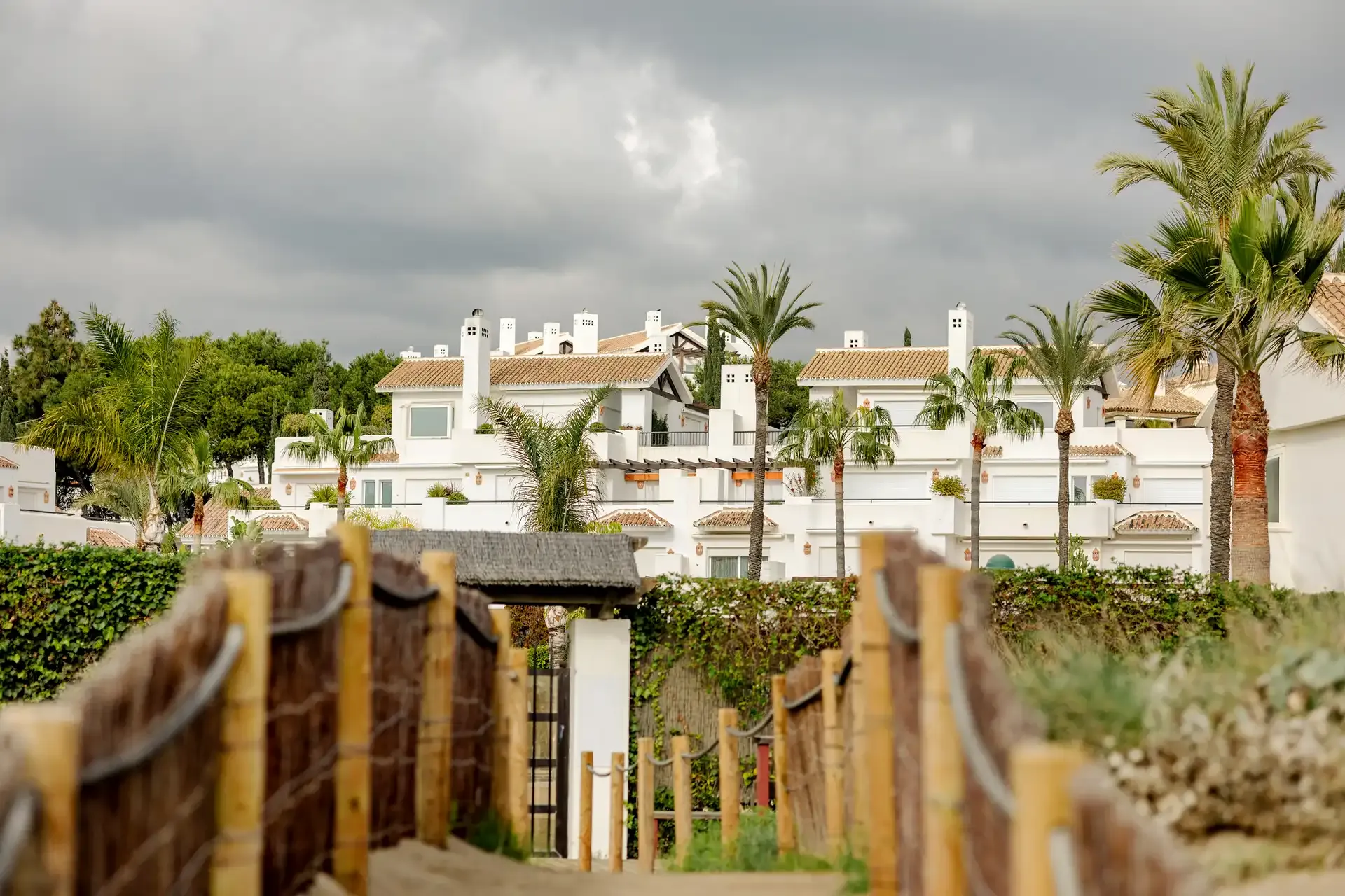A wooden garden gate opening from white beachfront houses onto the sand in Marbella