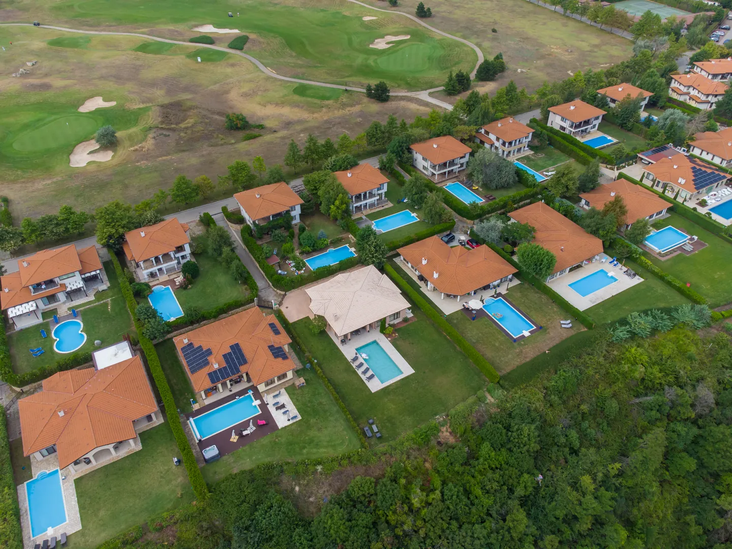 Aerial view of villas with terracotta roofs and pools beside a golf course