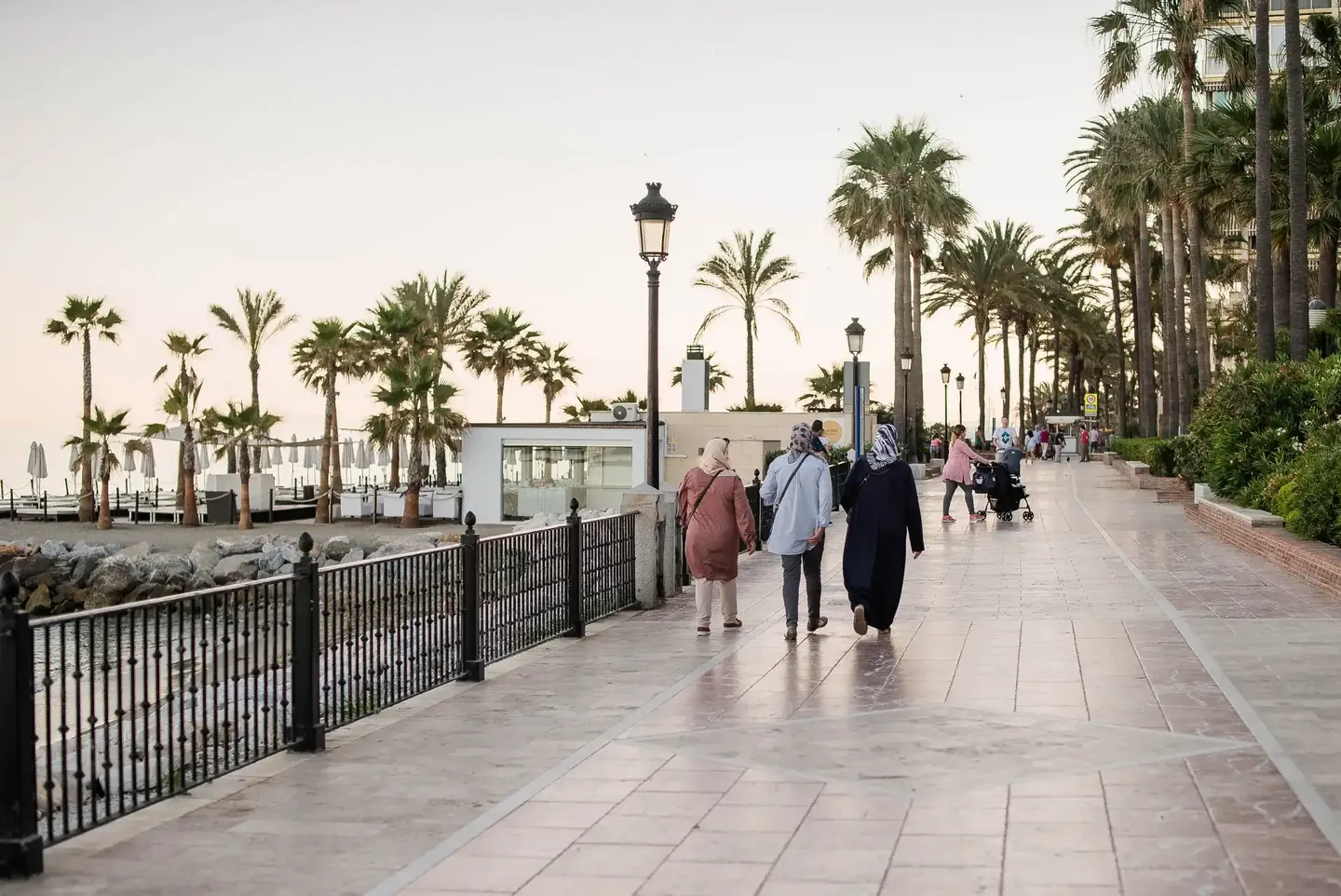 People walking along the palm-lined seafront promenade of Marbella