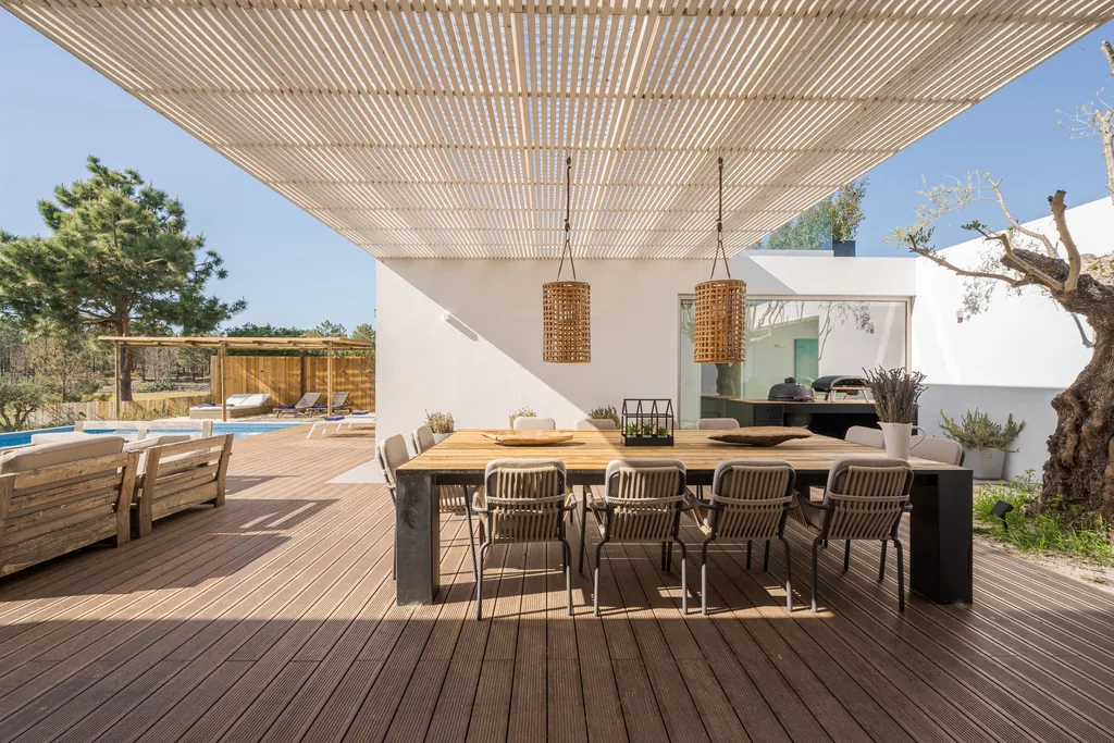 Long outdoor dining table under a slatted pergola beside the garden