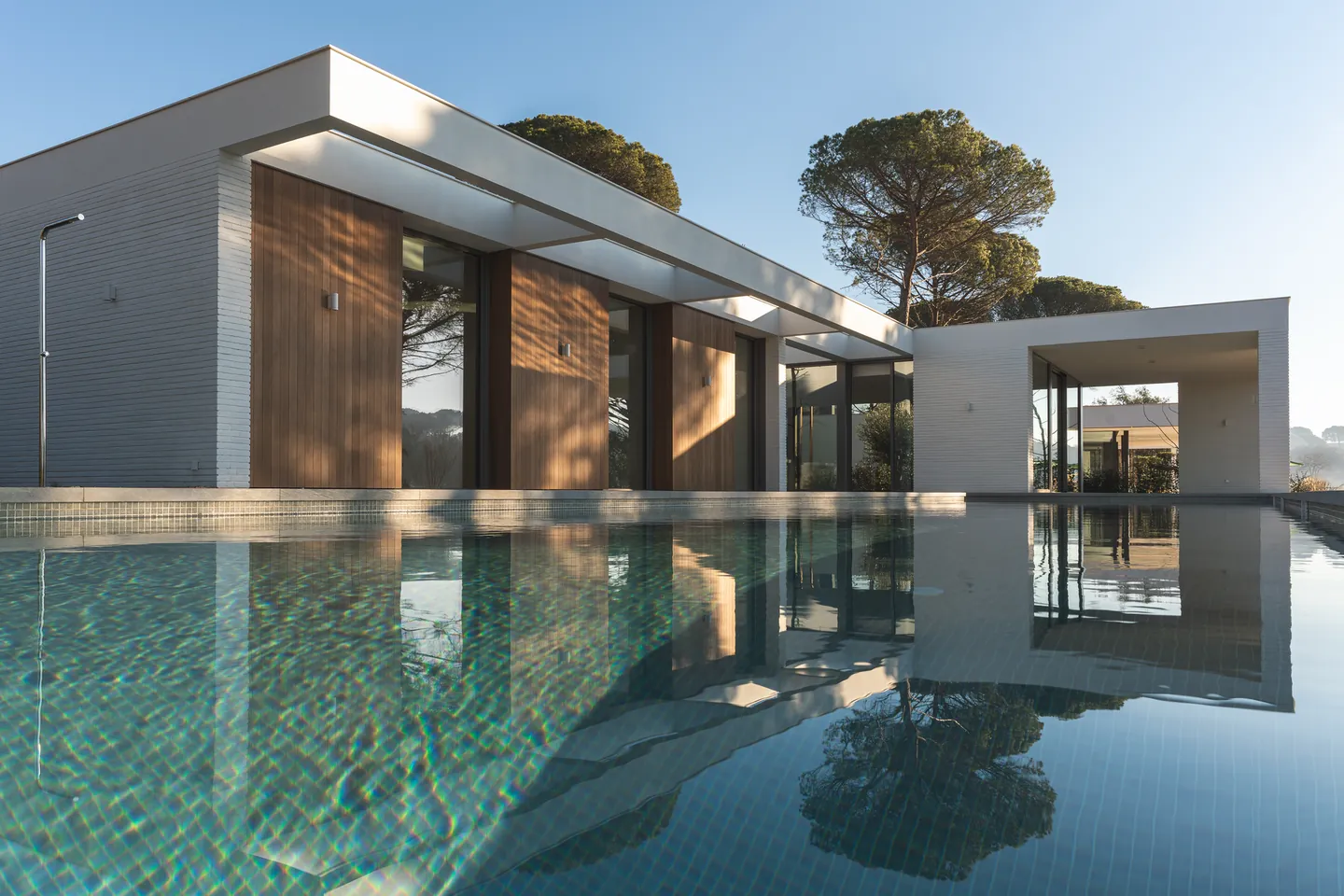 White villa with timber cladding reflected in a still pool